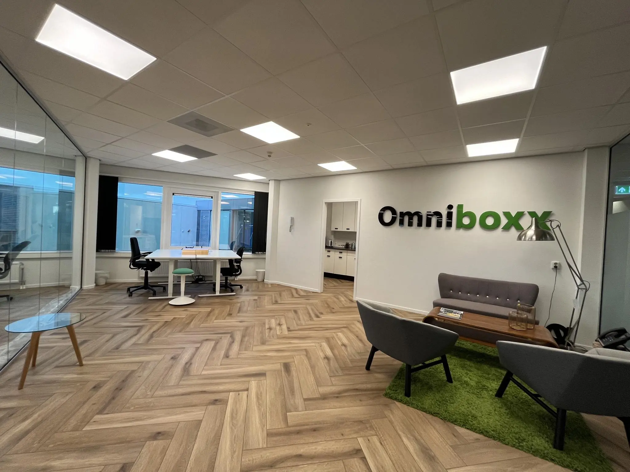 Moderne kantoorruimte van Omniboxx met een zithoek, vergadertafel en houten visgraatvloer.